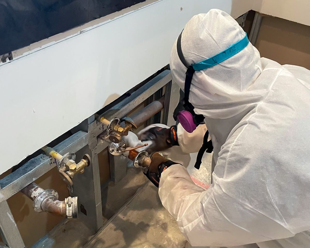 PPE technician with respirator working on pipe repair during odor remediation