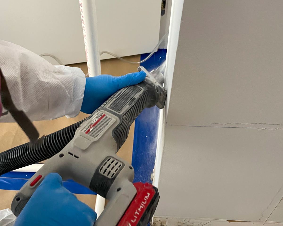 White-gloved hands operating oscillating tool on wall during treatment