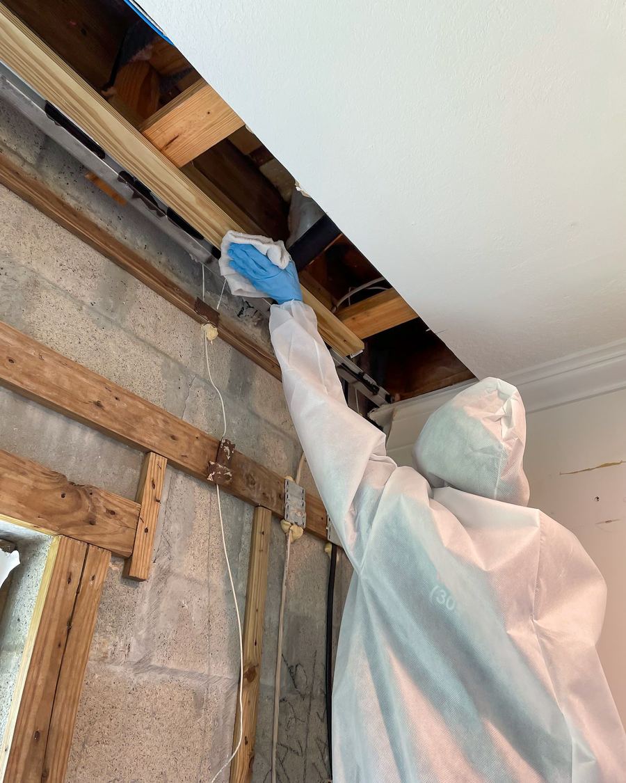 White-suited specialist reaching into ceiling space during remediation