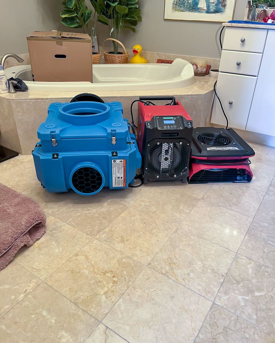 Professional dehumidification equipment, blue air scrubber, red dehumidifier, and flat air mover deployed in bathroom