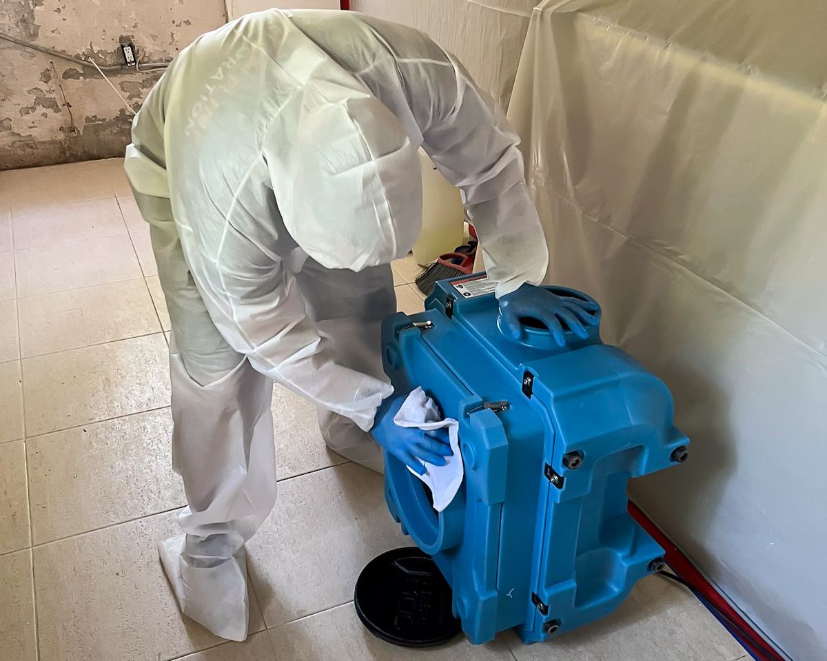 White-suited specialist positioning blue air mover during odor treatment
