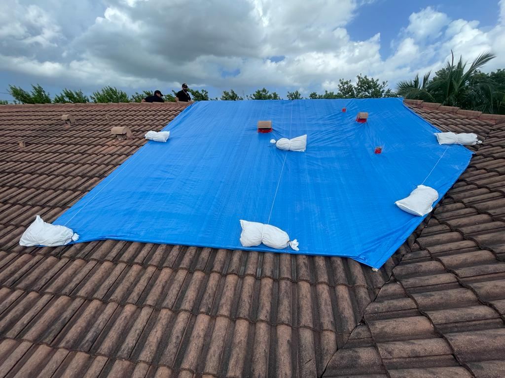 Frontline Restoration crew laying blue tarp across tile roof, stormy sky